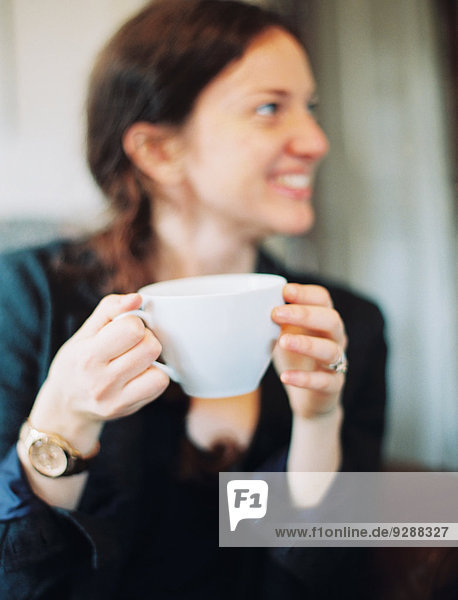 A woman holding a large white china cup and looking sideways smiling.