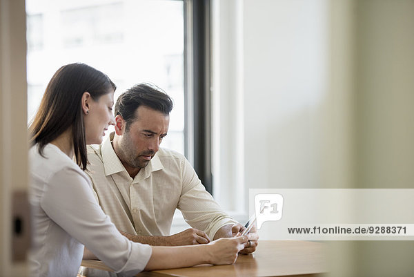 Ein Mann und eine Frau in einem Büro  die sich ein digitales Tablet teilen.