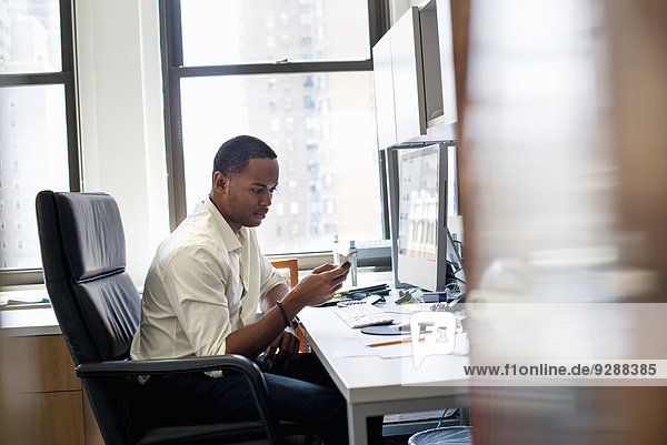 A man sitting in an office  checking his smart phone.