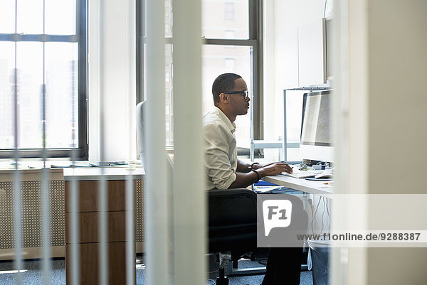Ein Mann  der in einem Büro arbeitet und an einem Schreibtisch sitzt. Er schaut auf einen Computerbildschirm.