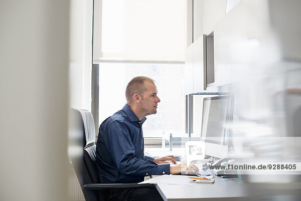 Ein Mann  der in einem Büro an einem Schreibtisch mit einer Computermaus arbeitet. Er konzentriert sich auf eine Aufgabe.