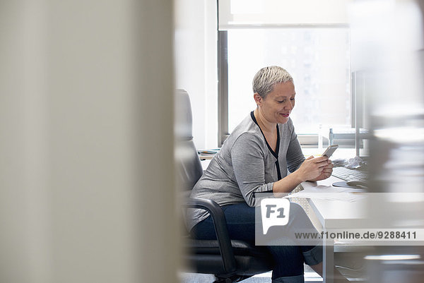 Eine Frau  die allein in einem Büro arbeitet und ihr Smartphone überprüft.