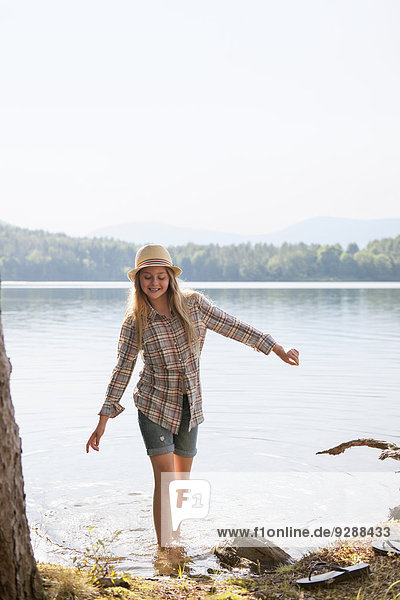 Ein Mädchen mit Strohhut paddelt im seichten Wasser eines Bergsees.
