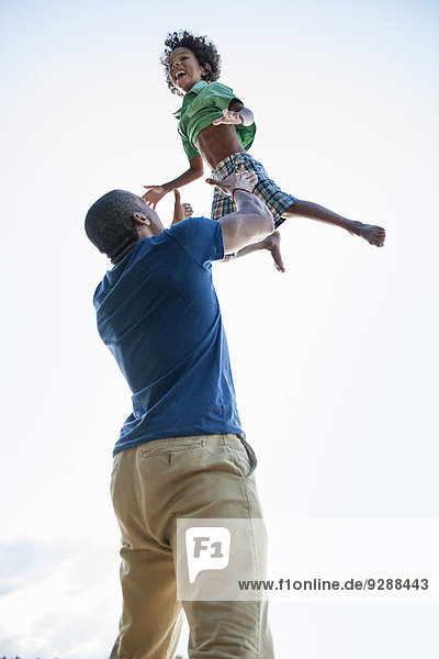 A man lifting a small boy up above his head in play.