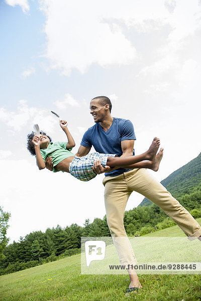 A man lifting his son up in his arms  playing outdoors.