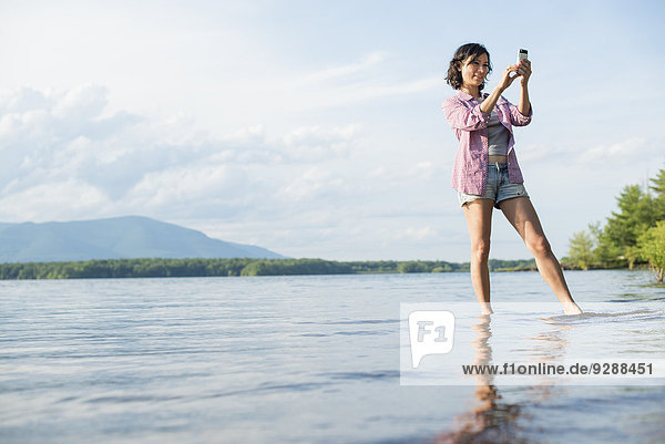 Eine Frau  die im Sommer in einem See steht. Sie macht ein Foto.