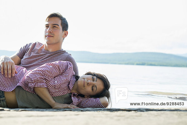 Ein Paar  das sich im Sommer auf einem Holzsteg an einem See entspannt.