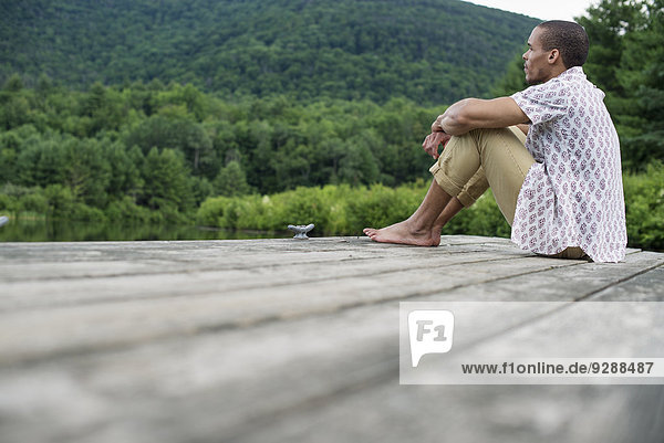 Ein Mann sitzt im Sommer auf einem Holzsteg an einem See