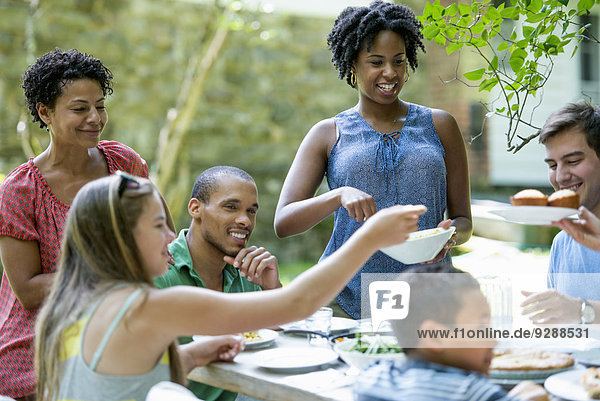 Ein Familientreffen  Männer  Frauen und Kinder um einen Tisch in einem Garten im Sommer.