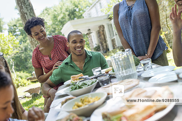 Ein Familientreffen  Männer  Frauen und Kinder um einen Tisch in einem Garten im Sommer.