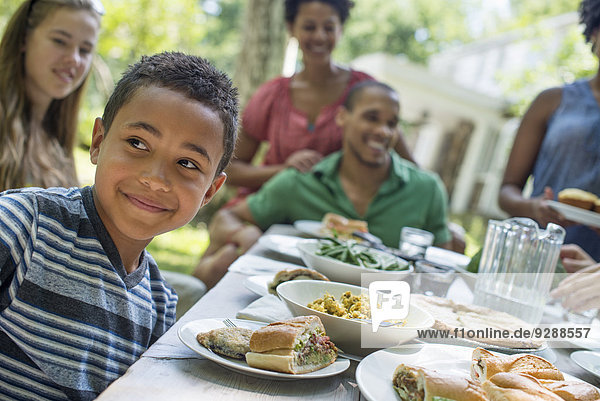 Ein Familientreffen  Männer  Frauen und Kinder um einen Tisch in einem Garten im Sommer. Im Vordergrund ein lächelnder Junge.