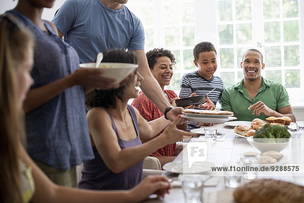 Ein Familientreffen  bei dem Männer  Frauen und Kinder an einem Esstisch sitzen und gemeinsam essen.