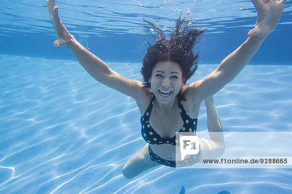 A woman with long black hair wearing a spotted bikini underwater.