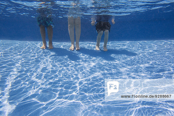Drei Personen  die auf dem Boden eines Schwimmbeckens stehen. Blick von den Knien nach unten.