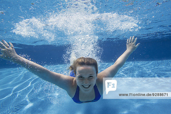 A young girl with long hair fanning out in the water swimming underwater.