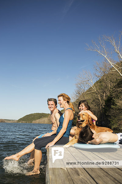 Eine Familie und ihr Apportierhund auf einem Steg an einem See.