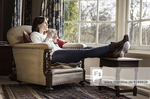Eine junge Frau  die sich zu Hause entspannt  die Füße hochgelegt und eine Tasse Tee trinkt.