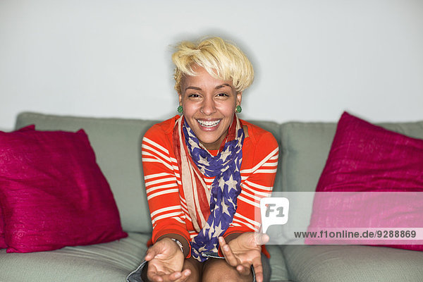 Eine Frau mit blonden Haaren sitzt lächelnd auf einem Sofa.