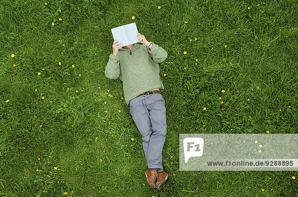 Ein Mann liegt auf dem Rücken im Gras und liest ein Buch.