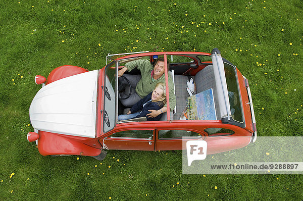 Blick von oben auf zwei Personen  ein Paar in einem Auto mit geöffnetem Dach.
