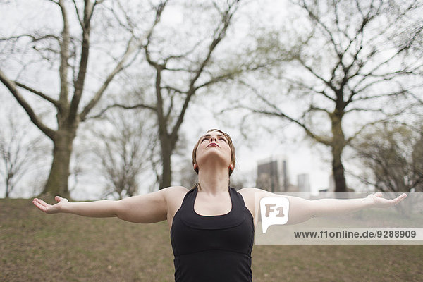 Eine junge Frau im Central Park in einem schwarzen Trikot und Leggings  die Yoga macht.