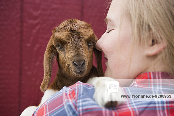 A girl cuddling a baby goat.