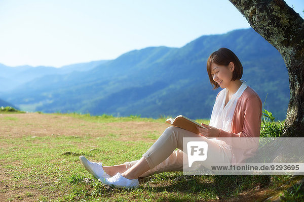 Young Japanese woman sitting with book in the countryside