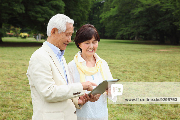 Senior adult Japanese couple with tablet in a park