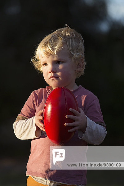 Süßer Junge schaut weg,  während er draußen einen Fußball hält.