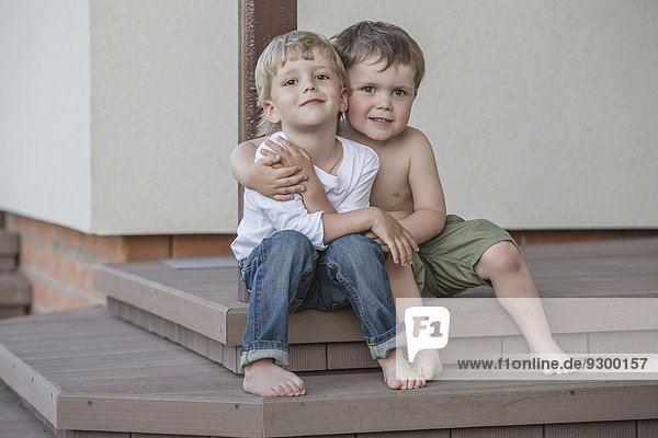 Ganzflächiges Porträt von Jungen  die auf der Veranda sitzen