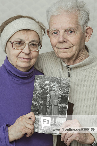 Porträt eines älteren Paares  das ein Bild von sich selbst in den Zwanzigern hochhält.