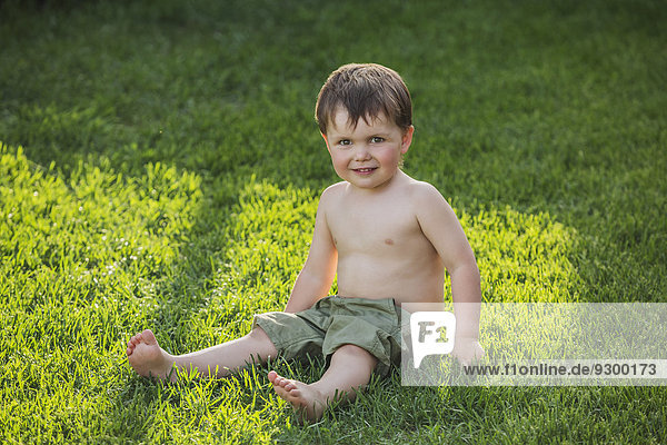 Porträt des süßen Jungen auf Gras sitzend