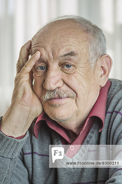 Porträt eines besorgten älteren Mannes mit der Hand auf dem Gesicht zu Hause