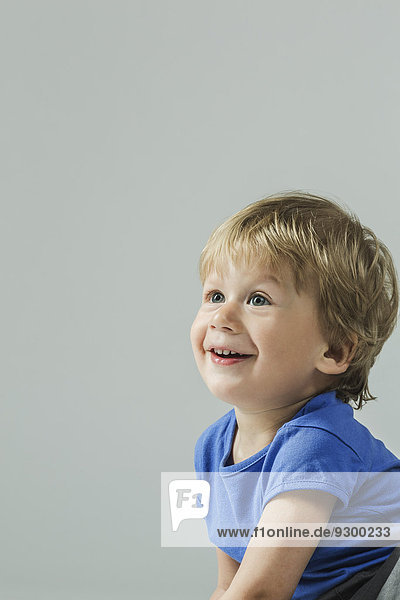 Lächelnder kleiner Junge  der über den grauen Hintergrund schaut.