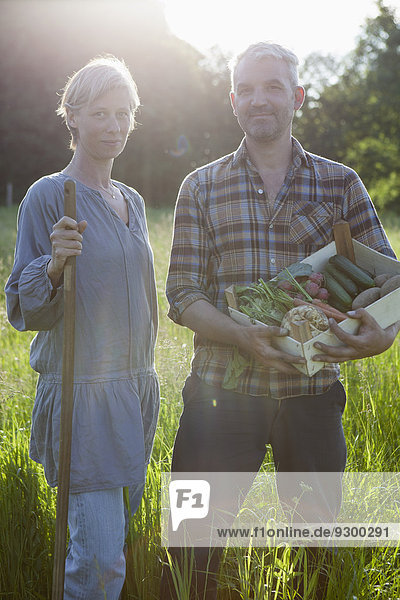 Porträt eines reifen Paares mit einer Kiste frisch geernteten Gemüses im Gemeinschaftsgarten