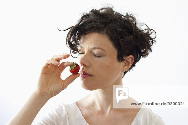 Eine Frau  die Erdbeere auf weißem Hintergrund riecht.
