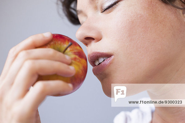 Abgeschnittenes Bild einer Frau  die Apfel über grauem Hintergrund riecht.