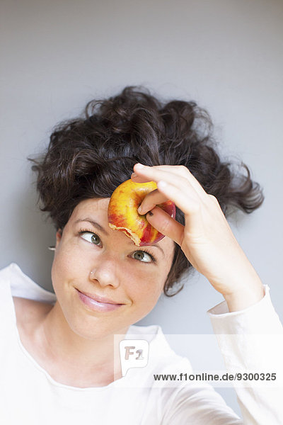 Eine Frau hält einen Apfel auf der Stirn über grauem Hintergrund.
