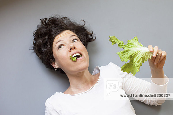 Eine Frau schaut weg  während sie Salat über grauem Hintergrund isst.