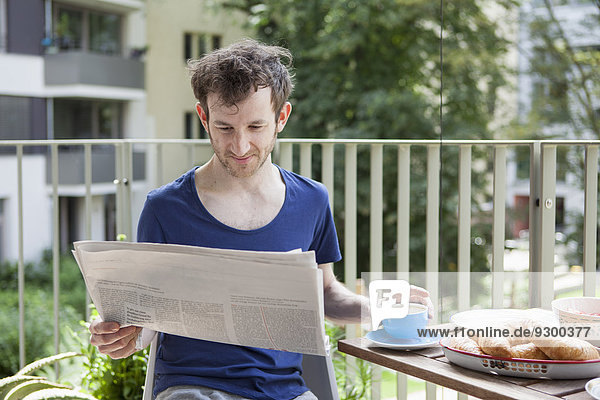 Young man reading newspaper while having breakfast at porch