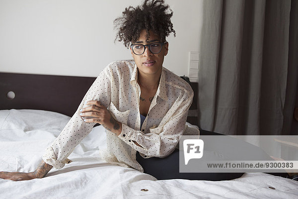 Thoughtful woman with curly hair sitting on bed at home