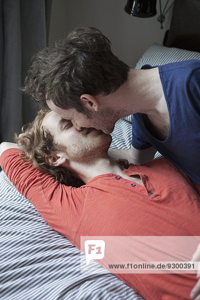 Junges schwules Paar beim Küssen im Schlafzimmer