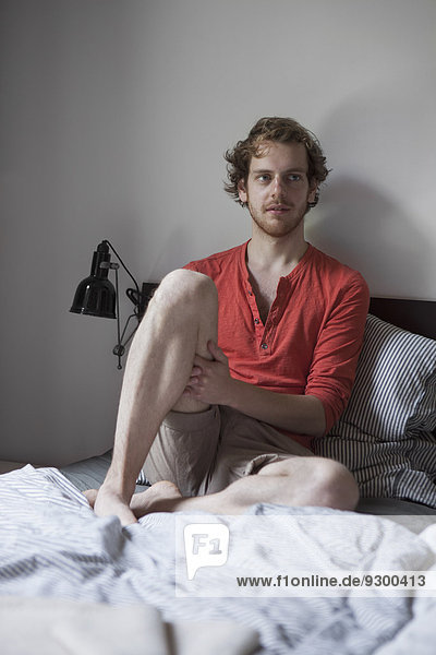 Young man sitting on bed at home