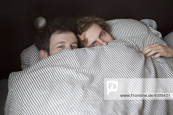 High angle portrait of young gay couple peeking through sheet in bed