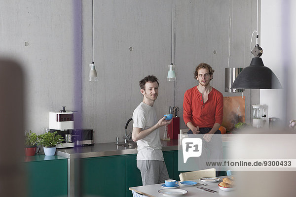 Young gay couple looking away in kitchen