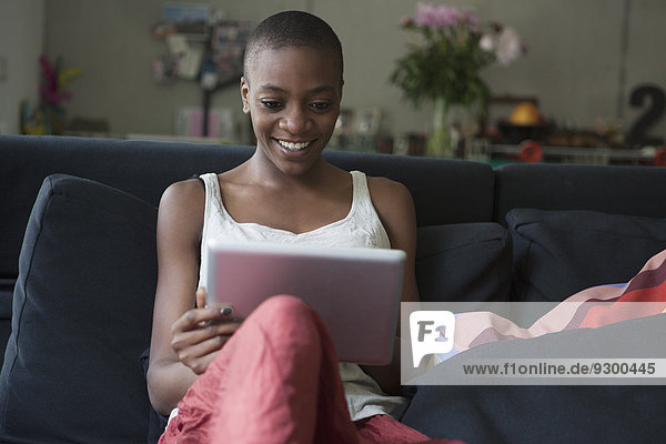 Lächelnde junge Frau mit digitalem Tablett auf dem Sofa zu Hause