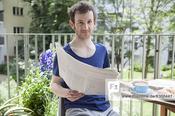Porträt eines jungen Mannes  der beim Kaffee auf der Veranda Zeitung liest.