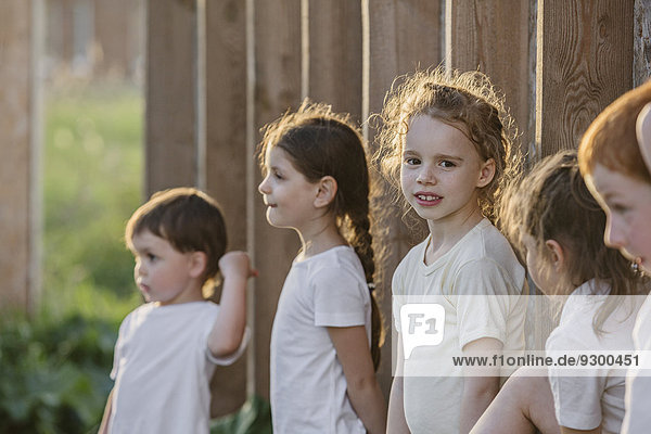 Porträt eines süßen Mädchens  das mit Freunden an einer Holzwand im Park steht.