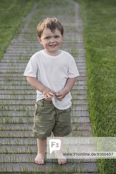 Porträt eines süßen Jungen  der auf einem Fußweg im Park steht.