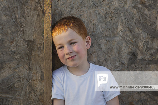 Porträt eines Jungen  der sich auf eine Holzbohle stützt.
